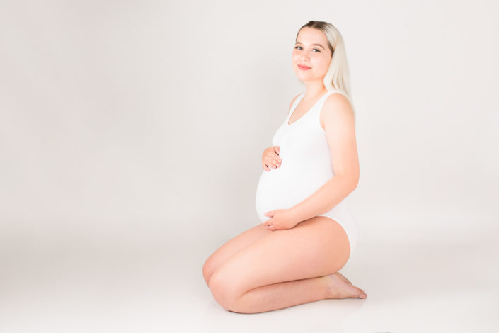 A pregnant lady kneels on her knees and looks up at the camera A pregnant lady kneels on her knees and looks up at the camera