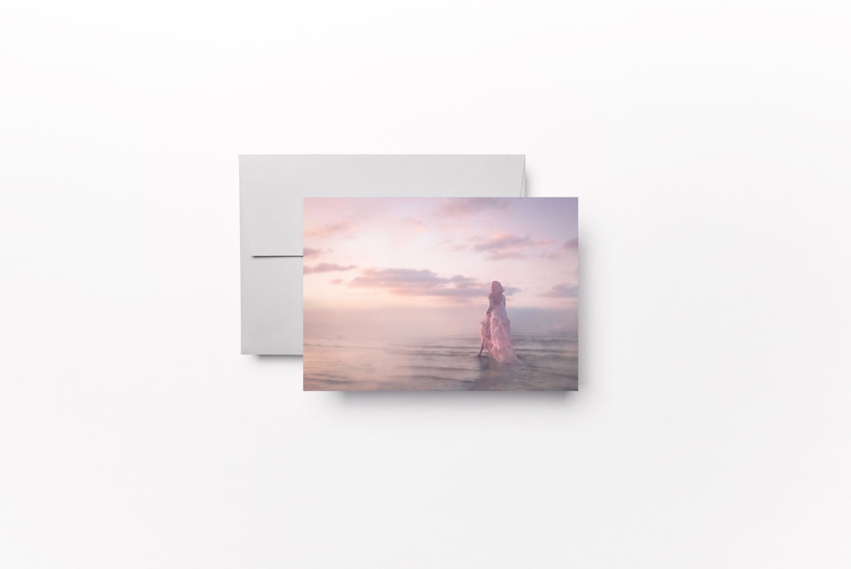 Elegant card with a woman in a pink dress at the beach during sunset.