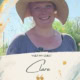 Smiling woman in a straw hat outdoors with blue sky and trees behind her.